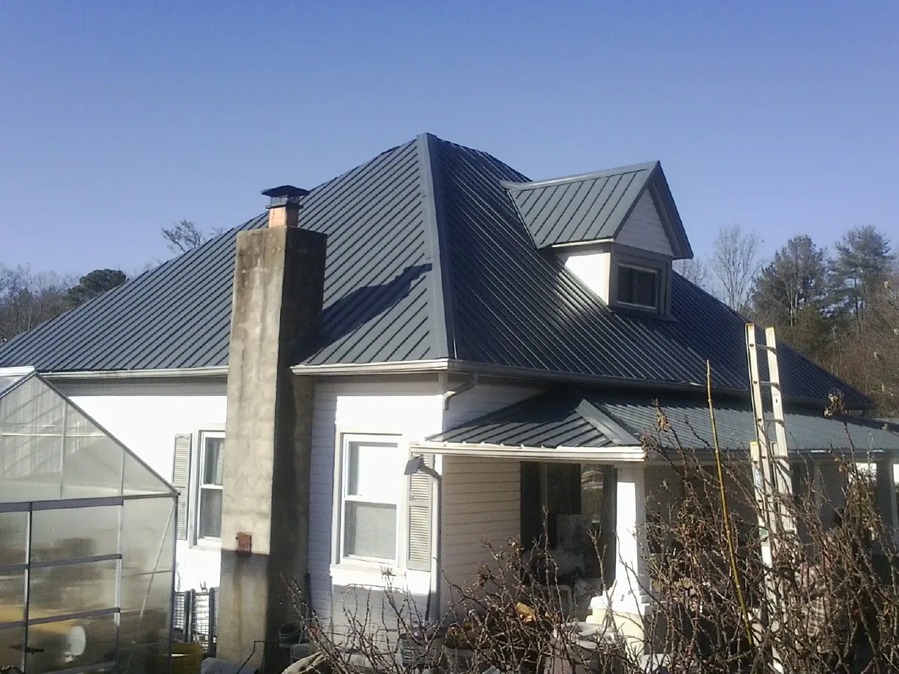 Dark blue standing seam metal roof on a white farmhouse with dormer — Slate & Tile Roof Repair by Roofing Brothers in Burr Hill
