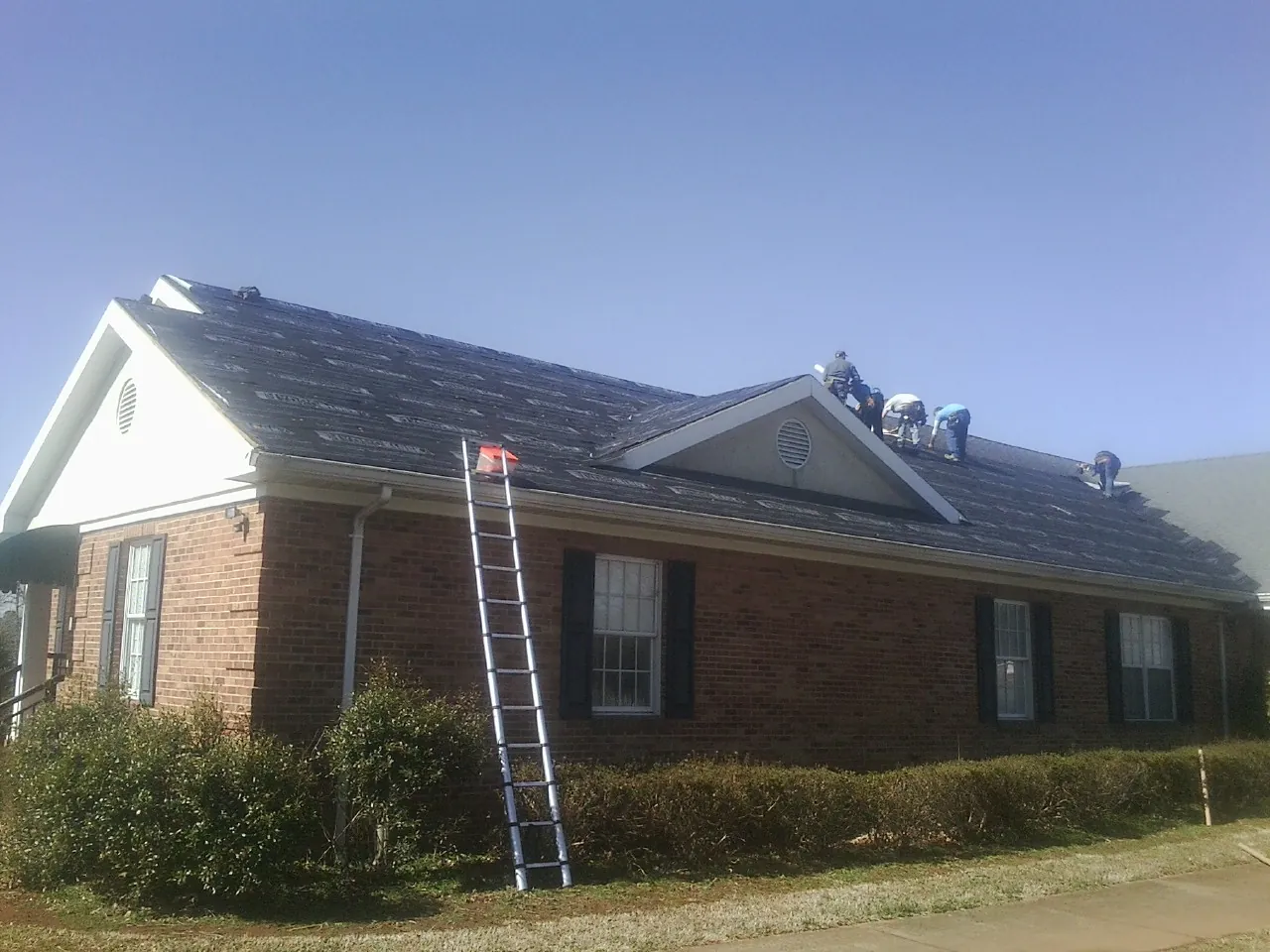 Crew tearing shingles off a brick ranch roof with a ladder set — Emergency Roof Repair work by our crew in Burr Hill