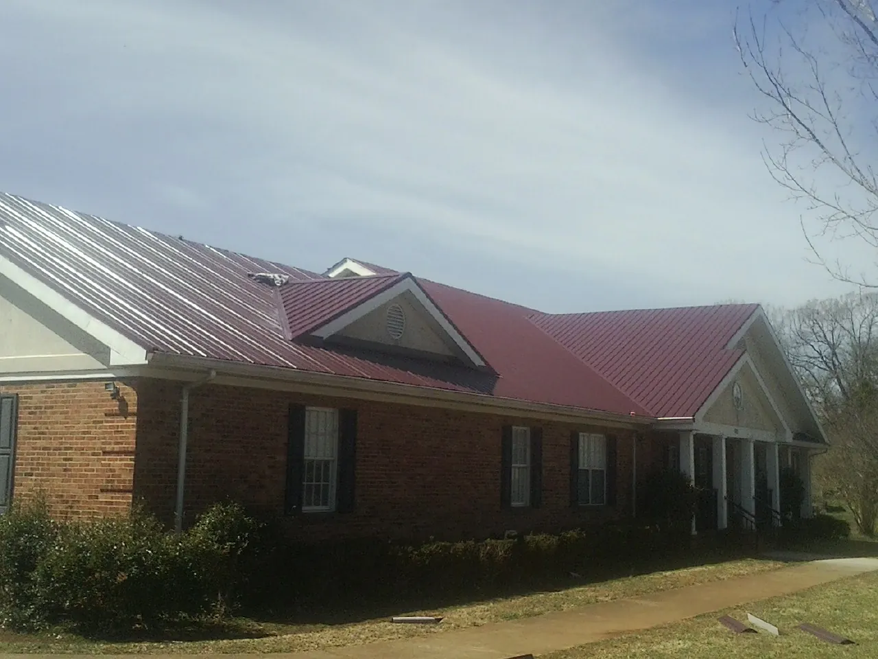 Red metal roof with gabled entries on a long brick building, from a Hail Damage Roof Repair job in Burr Hill