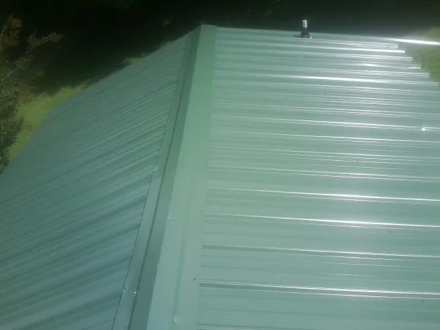 New green metal panels meeting at the ridge of a roof — Flat Roof Repair work by our crew in Burr Hill