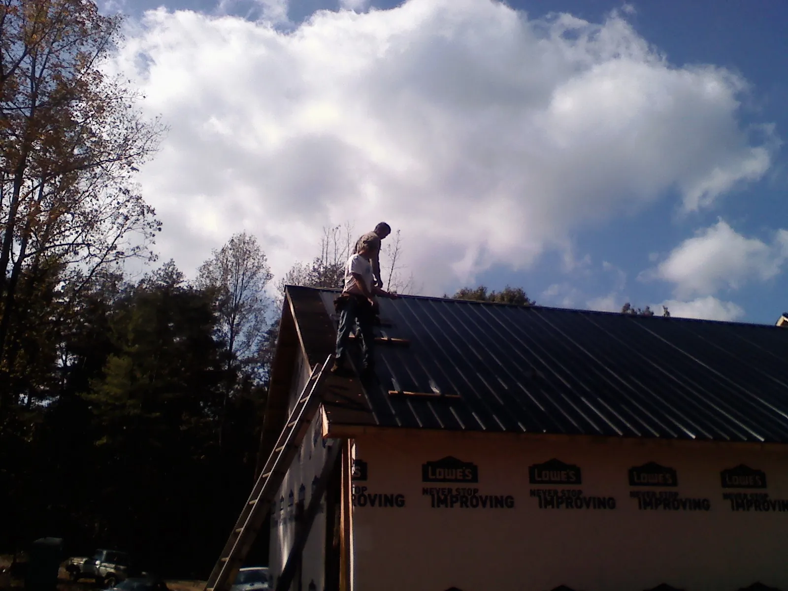 Roofer fastening dark metal panels high against a cloudy sky, from a Roof Inspection job in Burr Hill