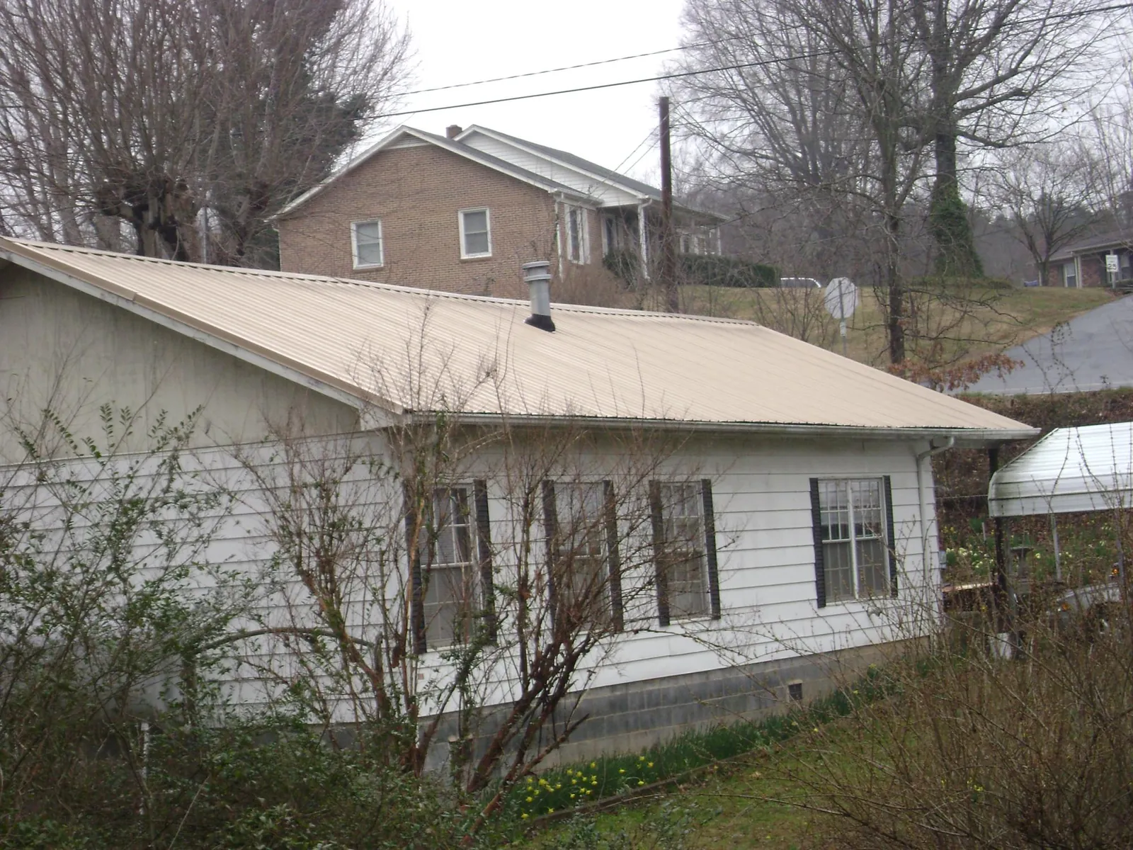 Tan metal roof on a white sided house set into a hillside — Commercial Roofing by Roofing Brothers in Burr Hill