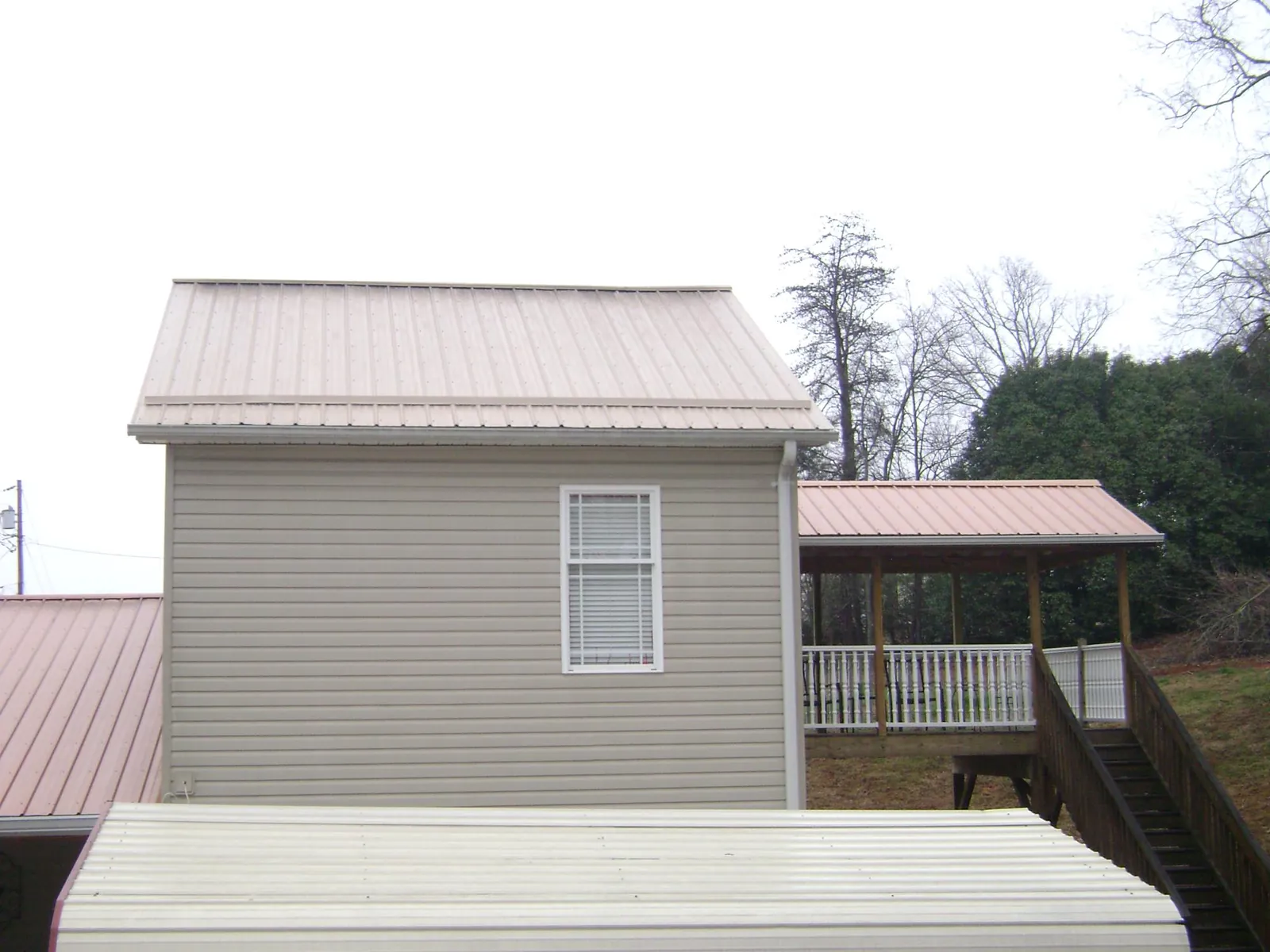 Tan metal roofs on a two story addition and attached porch, from a Roof Replacement job in Burr Hill